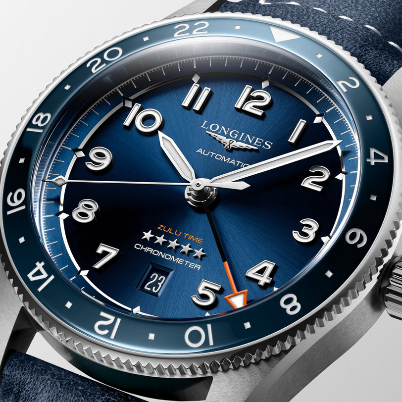 Close-up of the Longines Spirit Zulu Time wristwatch featuring a blue dial, blue ceramic bezel, silver hour markers, a 6 o’clock date window, and an orange-tipped GMT hand in a stainless steel case.