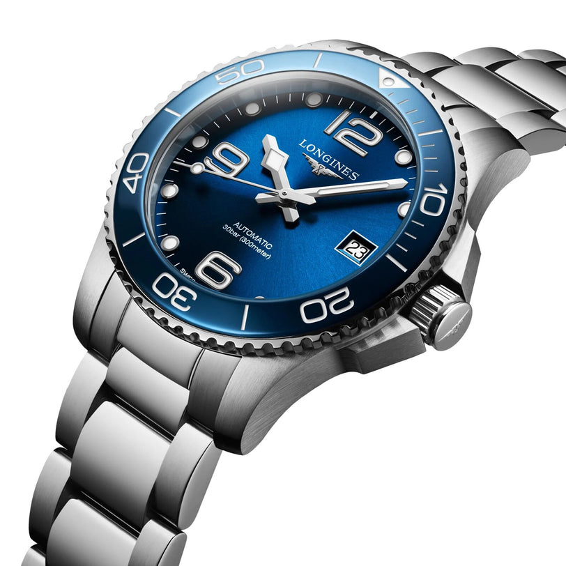 The Longines HydroConquest is a stainless steel wristwatch with a sunray blue dial and bezel, date display, prominent numerals, and a metal link bracelet.