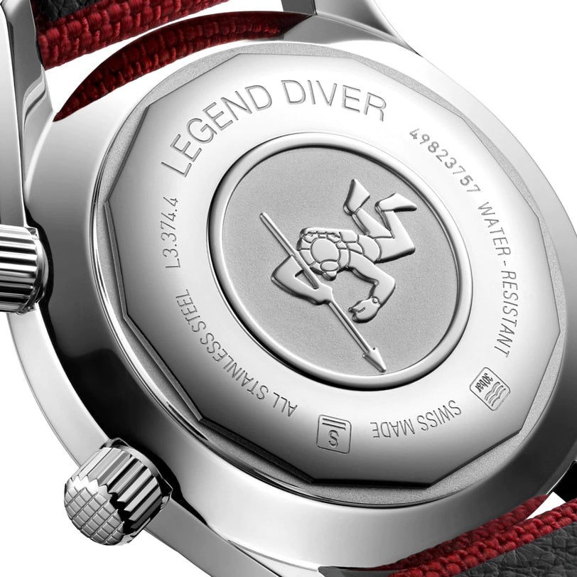 Close-up of the Longines Legend Diver’s case back displays engraved text and a diving figure emblem, featuring a stainless steel finish and a red-black strap detail.