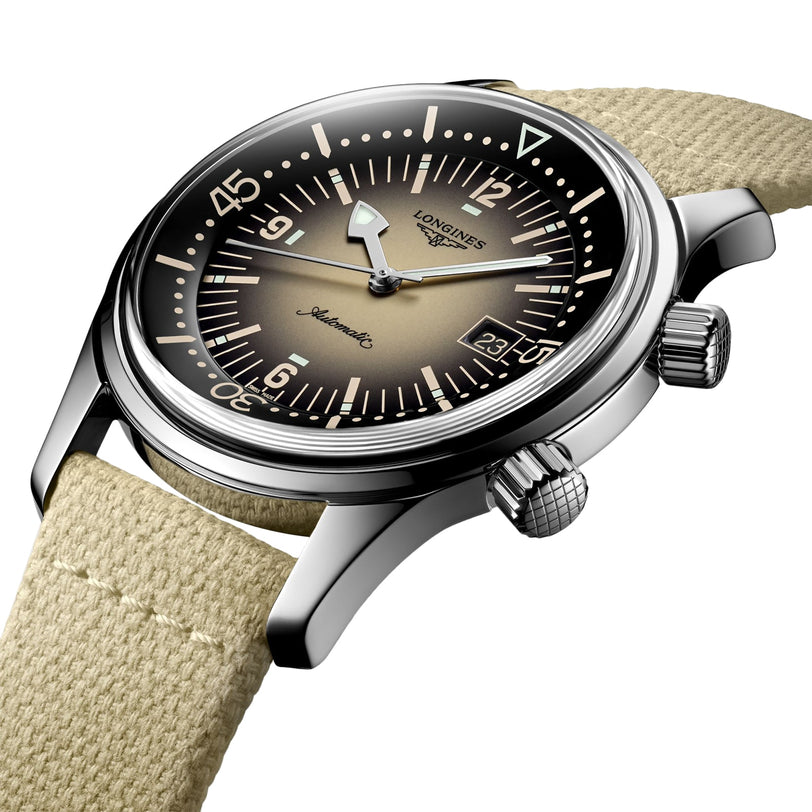 A close-up of the Longines Legend Diver featuring a beige gradient dial, date display, dual crowns, L888 calibre movement, and a light beige fabric strap.