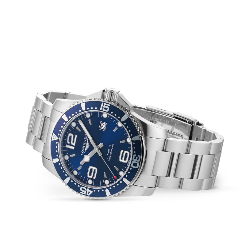 The Longines HydroConquest wristwatch features automatic movement, a blue dial with silver markers, and a date window. Part of the Sport Collection, it is crafted in stainless steel and shown on a white background.