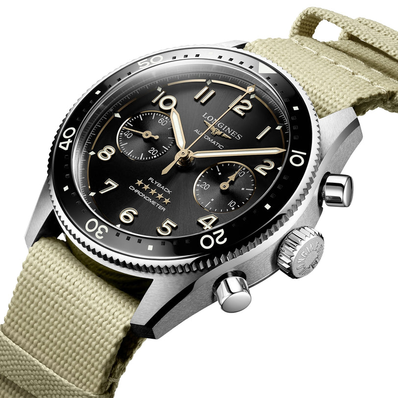 Close-up of the Longines Spirit Flyback wristwatch featuring a black dial, three subdials, silver bezel, and beige fabric strap. This chronometer offers time, chronograph, and tachymeter functions with automatic calibre L791.