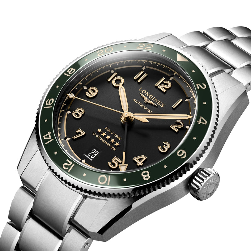 A close-up of the Longines Spirit Zulu Time watch, featuring a green ceramic bezel, black dial, gold-tone numerals, and a stainless steel bracelet.