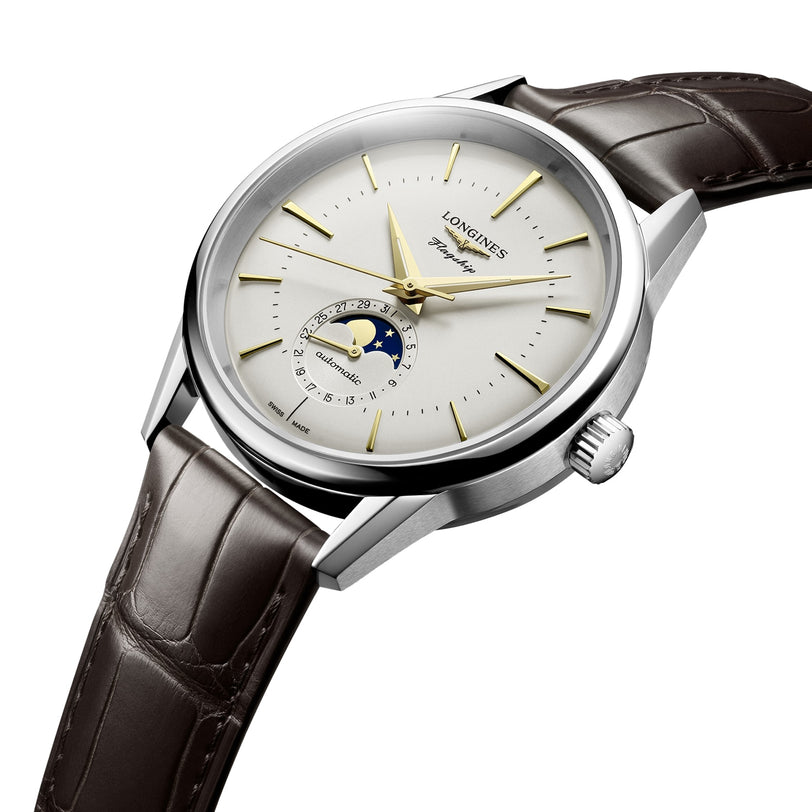 The Longines Flagship Heritage Moonphase features a silver case, white dial, gold hands, date pointer, moon phase display, and brown leather strap—embodying innovative spirit with timeless design.