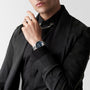 A person in a black suit and shirt with a chain necklace showcases the Longines Legend Diver watch, featuring automatic movement and a dark dial, on their left wrist.