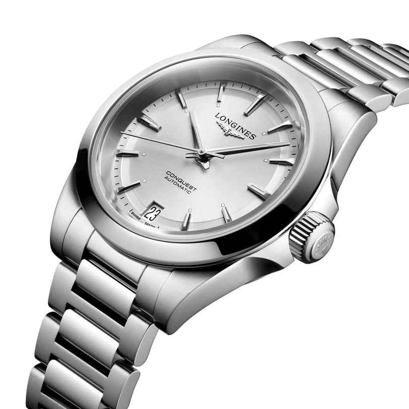 The Longines Conquest features an automatic movement, stainless steel case, silver dial with index markers, date at 6 o’clock, and a metal bracelet.