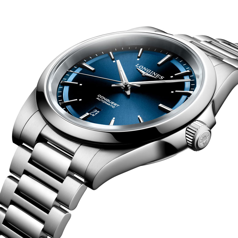 The Longines Conquest stainless steel watch features a sunray blue dial, silver hour markers, date window at 3 o’clock, and a metal link bracelet, displayed on a white background.