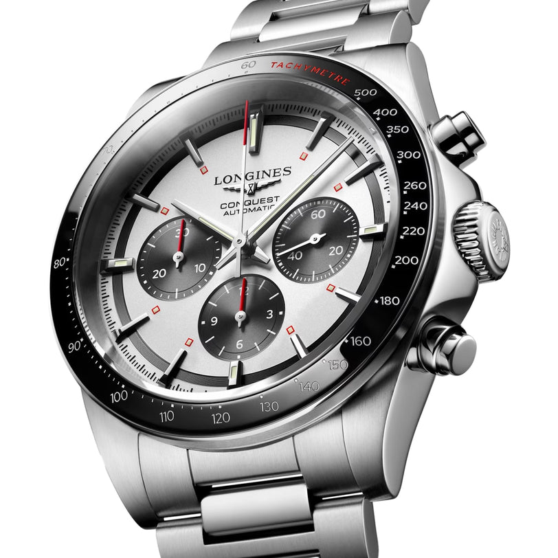 The Longines Conquest Chronograph features a stainless steel case, silver dial with three subdials, black tachymeter bezel, self-winding movement, and a metal bracelet.