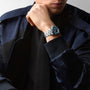 A person in a dark jacket and black shirt rests their chin on their hand, showcasing the Longines HydroConquest diving watch with a blue face and stainless steel case.
