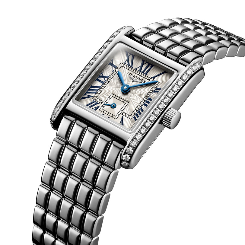 The Longines Mini DolceVita features a rectangular stainless steel case, metal link band, blue Roman numerals and hands, a small seconds dial, and a bezel adorned with Top Wesselton diamonds.
