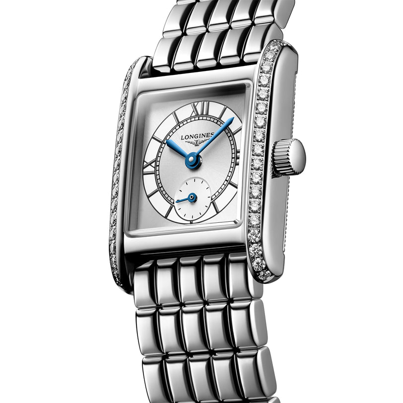 The Longines Mini DolceVita is a rectangular silver wristwatch with a white dial, blue hands, Roman numerals, a diamond-set bezel with Top Wesselton diamonds, and a stainless steel bracelet.