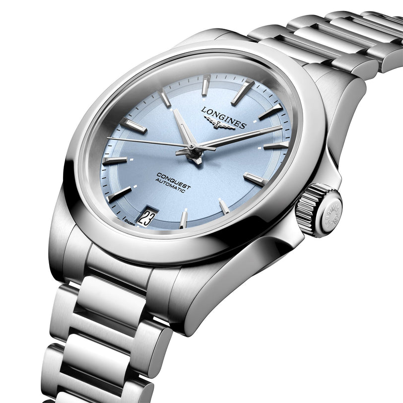 The Longines Conquest features a stainless steel case, automatic movement, light blue dial with silver hour markers, date at 6 oclock, and a metal bracelet.
