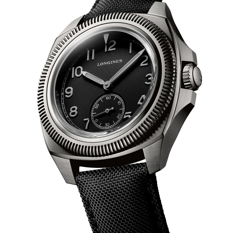 The Longines Pilot Majetek Pioneer Edition is a stainless steel wristwatch with a black dial, white numerals, small seconds subdial, fluted bezel, black fabric strap, and a precise silicon balance-spring for enhanced performance.