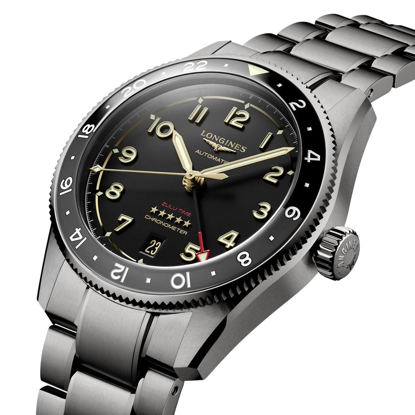 A close-up of the Longines Spirit Zulu Time, featuring a stainless steel band, black dial, gold-tone hands, and red accents on the 5 and GMT hand.