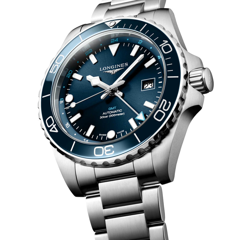 A Longines HydroConquest stainless steel automatic GMT dive watch with a blue bezel, blue dial, date display, and metal bracelet is shown at an angle on a white background.