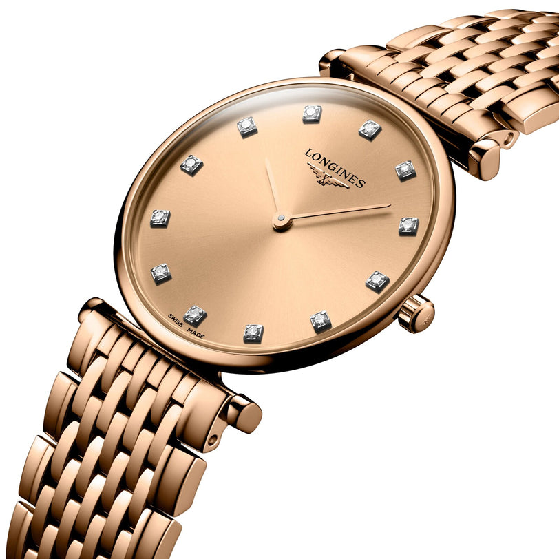 The La Grande Classique de LONGINES by Longines is a gold wristwatch featuring a woven metal band, diamond hour markers, and a minimalist round face with no numerals.