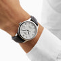 A person wearing a Tissot Le Locle Powermatic 80 with a white dial, black Roman numerals, and black leather strap, paired with a white long-sleeve shirt—a nod to classic Swiss style.