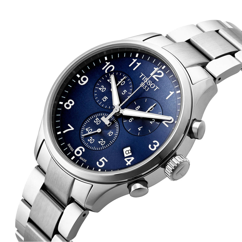 The Tissot Chrono XL Classic is a stainless steel chronograph watch featuring a blue dial with three subdials, date display, silver hour markers, and a metal bracelet.