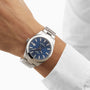 A person in a white long-sleeve shirt wears the Tissot Gentleman Powermatic 80 Silicium, featuring a blue dial, stainless steel case, and metal band.