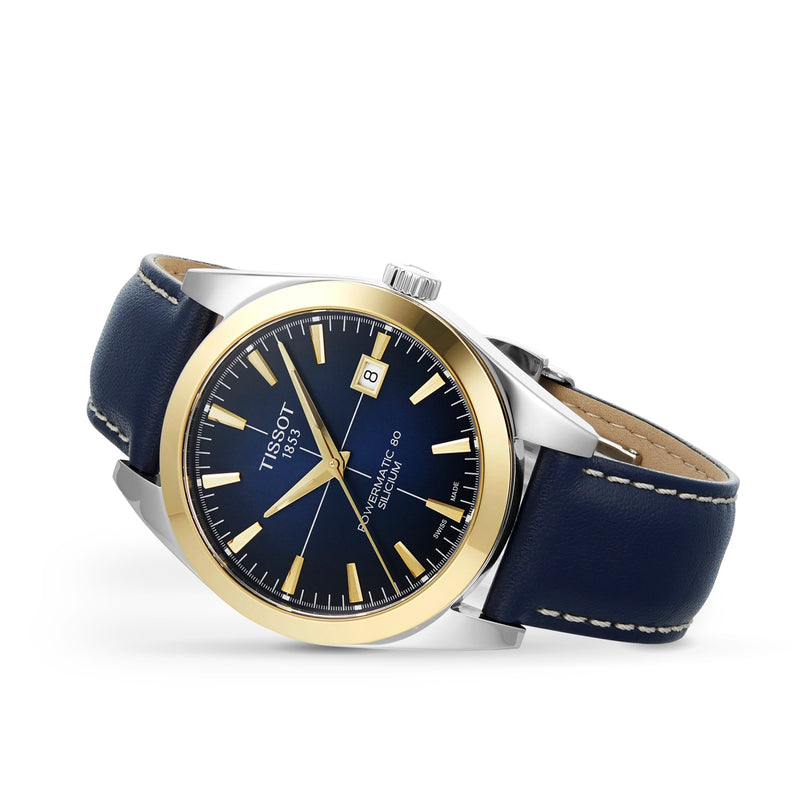 The Tissot Gentleman Powermatic 80 Silicium with a solid 18k gold bezel features a black dial, date display, and blue leather strap, blending luxury and style with renowned Powermatic 80 movement.