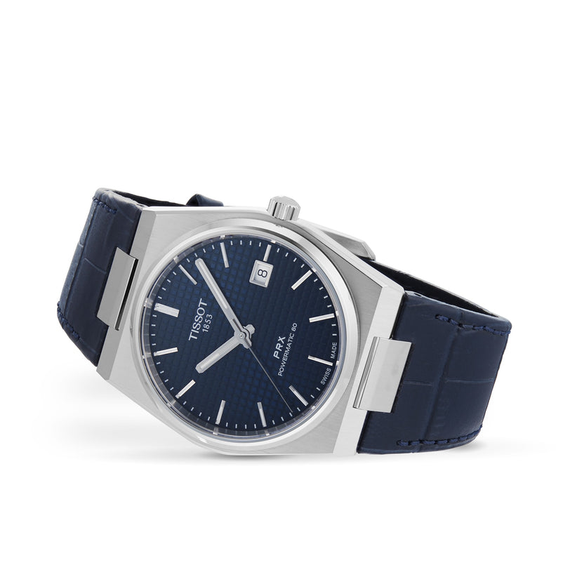 A Tissot PRX Powermatic 80 wristwatch featuring a blue textured dial, silver hour markers, stainless steel case, date display, and blue leather strap, shown against a white background.