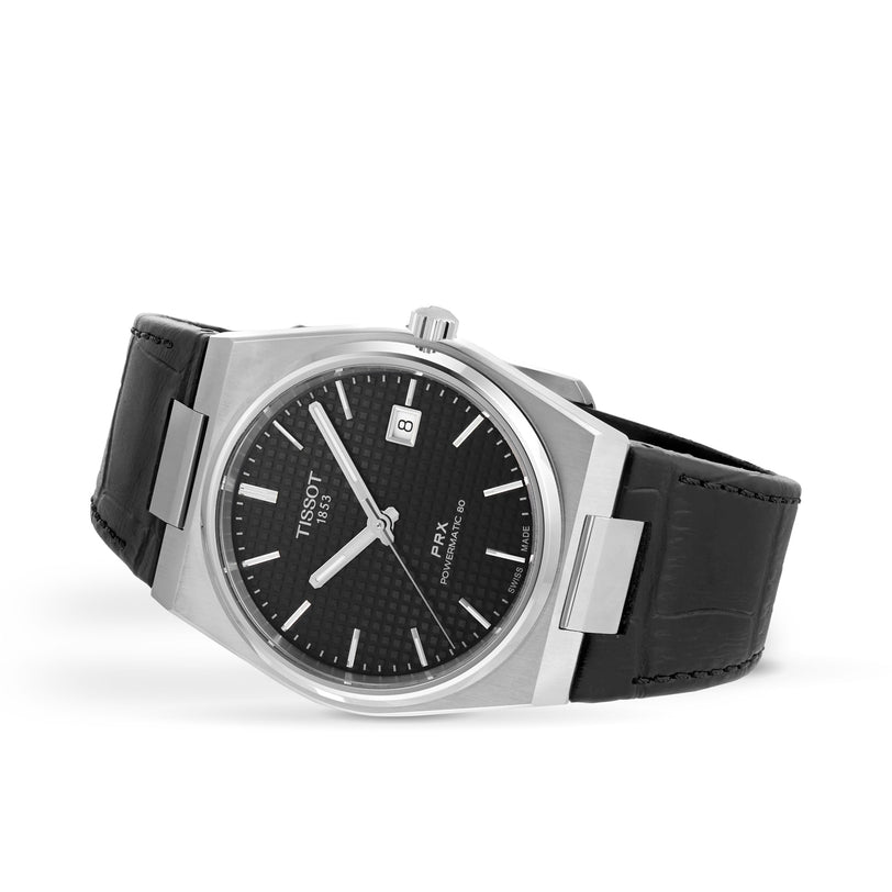 The Tissot PRX Powermatic 80 is a stainless steel wristwatch featuring a black textured dial, date window, silver hour markers, black leather strap, and a 1970s-inspired design in a sleek case.