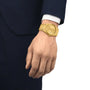 A person’s hand wearing a Tissot PRX Powermatic 80 watch is visible; they are dressed in a dark navy blue suit with a white shirt.