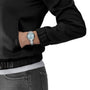 A person wearing a black jacket, gray pants, and a Tissot PR 100 silver wristwatch with a light blue face and Swiss Quartz movement on their left wrist.
