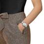 A person wearing Tissots PR 100 watch and brown pants with a hand in their pocket.