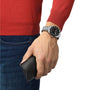 A person in a red sweater and jeans wears a Tissot PR516 Powermatic 80 silver wristwatch and holds a black case.