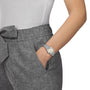 A person wearing gray pants and a white top with their left hand in their pocket, showcasing a Tissot PRX silver wristwatch known for its vintage aesthetic design.