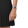 A person wears a black pleated skirt and a Tissot PRX 25mm silver wristwatch with a black dial and sapphire crystal, shown from the waist down against a white background.