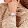 A person in a beige knit sweater rests their chin on their hand, showcasing a TAG Heuer Aquaracer Professional 200 with a white dial and metal band.