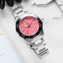 The TAG Heuer Aquaracer Professional 300 Date, featuring a silver stainless steel case, pink dial with diamond markers, and a black bezel inspired by classic dive watches, shines on a white surface beside a metal caliper and notebook.