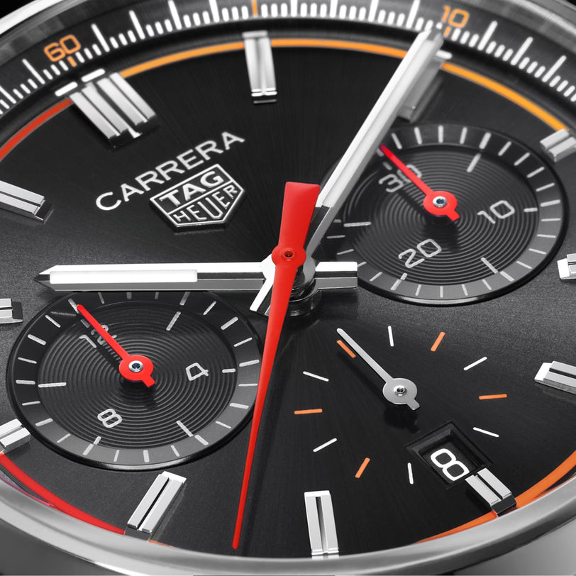 Close-up of the TAG Heuer Carrera Chronograph watch face with a black dial, three subdials, a date window, and red accents on the hands. Features precision Calibre HEUER 02 movement.