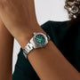 A person wearing a TAG Heuer Aquaracer Professional 200 watch with a green face and silver band holds their hands together near their face against a neutral background.
