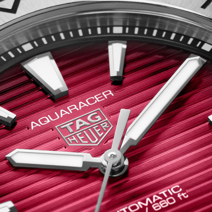 Close-up of a TAG Heuer Aquaracer Professional 200 watch face with a smokey-red sunray brushed dial, silver markers and hands, partial brand logo, AUTOMATIC 660 ft text, and a sleek stainless steel case.