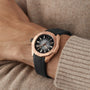 A person wears a TAG Heuer Aquaracer Professional 200 in rose gold with a black dial and black rubber strap on their left wrist above a beige knit sweater.