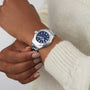 A person wearing a cream-colored knit sweater sports a TAG Heuer Aquaracer 200 Professional Solargraph, showcasing its silver case and blue dial.