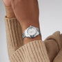 A person wears a TAG Heuer Aquaracer 200 Professional Solargraph silver sports watch with a white dial and stainless steel band, shown against a tan sweater sleeve.