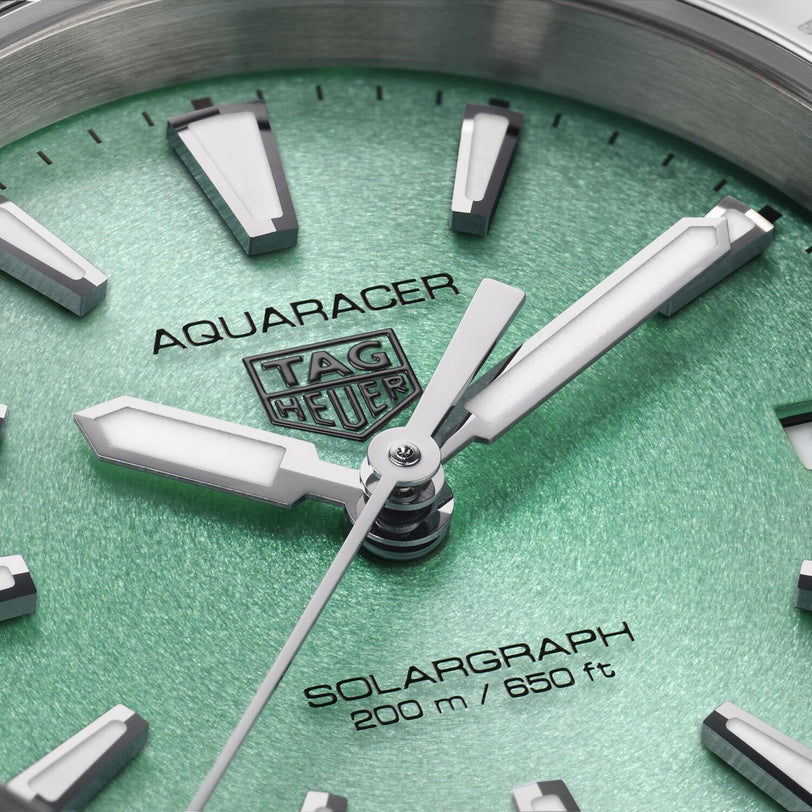 Close-up of the TAG Heuer Aquaracer 200 Professional Solargraph watch face set against a green textured background, featuring silver hour markers and hands inspired by the Northern Lights. Water resistant to 200 m / 650 ft.