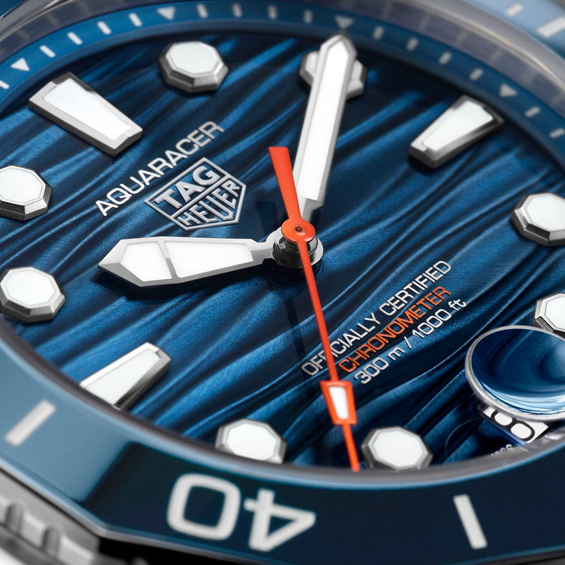 Close-up of the TAG Heuer Aquaracer Professional 300 Date watch face, highlighting its blue textured dial, white markers, red second hand, and Officially Certified Chronometer 300m / 1000ft text—emblems of Swiss craftsmanship.
