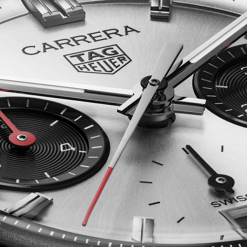 Close-up of the TAG Heuer Carrera Chronograph watch face, showcasing the Carrera logo, subdials, and silver hands with red tips under a scratch-resistant sapphire crystal.