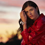Woman in a shiny red jacket poses outdoors at sunset, touching her hair and wearing a TAG Heuer Carrera Chronograph wristwatch.