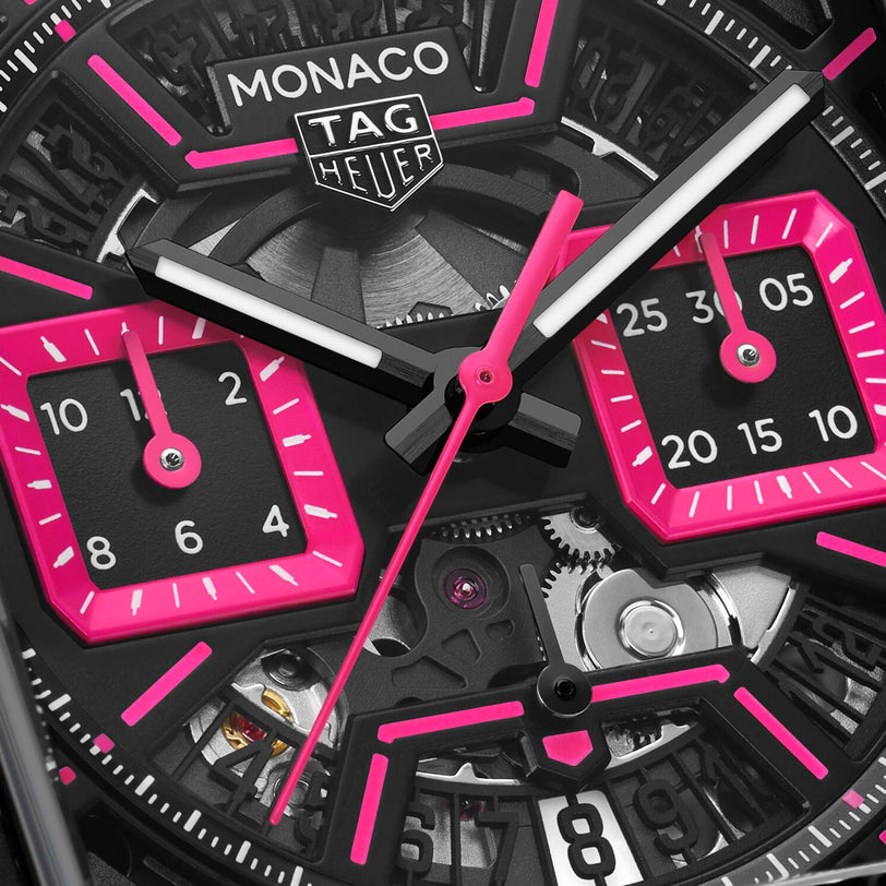 Close-up of the TAG Heuer Monaco Chronograph watch face, featuring black and hot pink details with visible gears and dials.