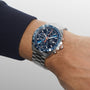 A TAG Heuer Formula 1 Chronograph wristwatch with a blue face, metal band, and blue ceramic tachymeter bezel is worn on a left wrist, showing the time and date.