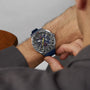 A person in a gray shirt adjusts a TAG Heuer Formula 1 Chronograph X Oracle Red Bull Racing, a motorsport-inspired watch, on their left wrist.