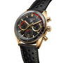 TAG Heuer Carrera Chronosprint x Porsche Rallye chronograph watch with a gold case, black dial, and leather strap, displayed at an angle.