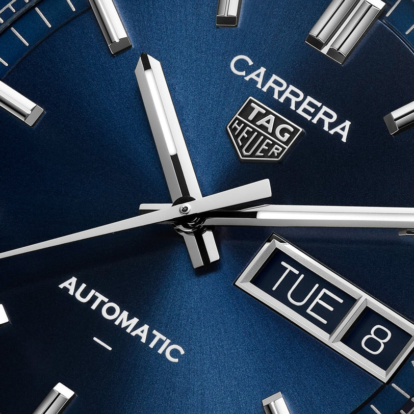 Close-up of the TAG Heuer Carrera Day-Date watch face displaying the hands, brand logo, and a date window showing TUE 8.
