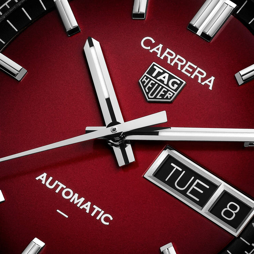 Close-up of a red TAG Heuer Carrera Day-Date watch face displaying Tuesday the 8th and showing the time near 10:10.